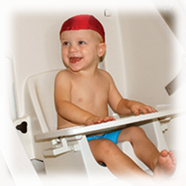 A toddler wearing a swim cap, seated in the Tod Pod chair insert with a tray across the lap
